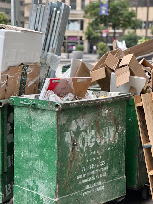 A large pile of black plastic rubbish bags, some tied at the top and others partially open, are stacked against a wall made of large, light-colored tiles. The bags contain mixed waste, with a few visible plastic bottles and miscellaneous debris protruding from the tops. Behind the pile, the wall features red graffiti spelling 'XEND' in spray paint, and nearby, an urban skyline with buildings and a cloudy sky is faintly visible. The scene appears to be outdoors, possibly on a street or alleyway, illustrating private or independent waste disposal involving on-site rubbish collection handled by companies such as Rubbish Removal Waterloo. The environment suggests an urgent or residual collection point for discarded waste, emphasizing the need for professional rubbish removal services to clear such accumulation effectively.